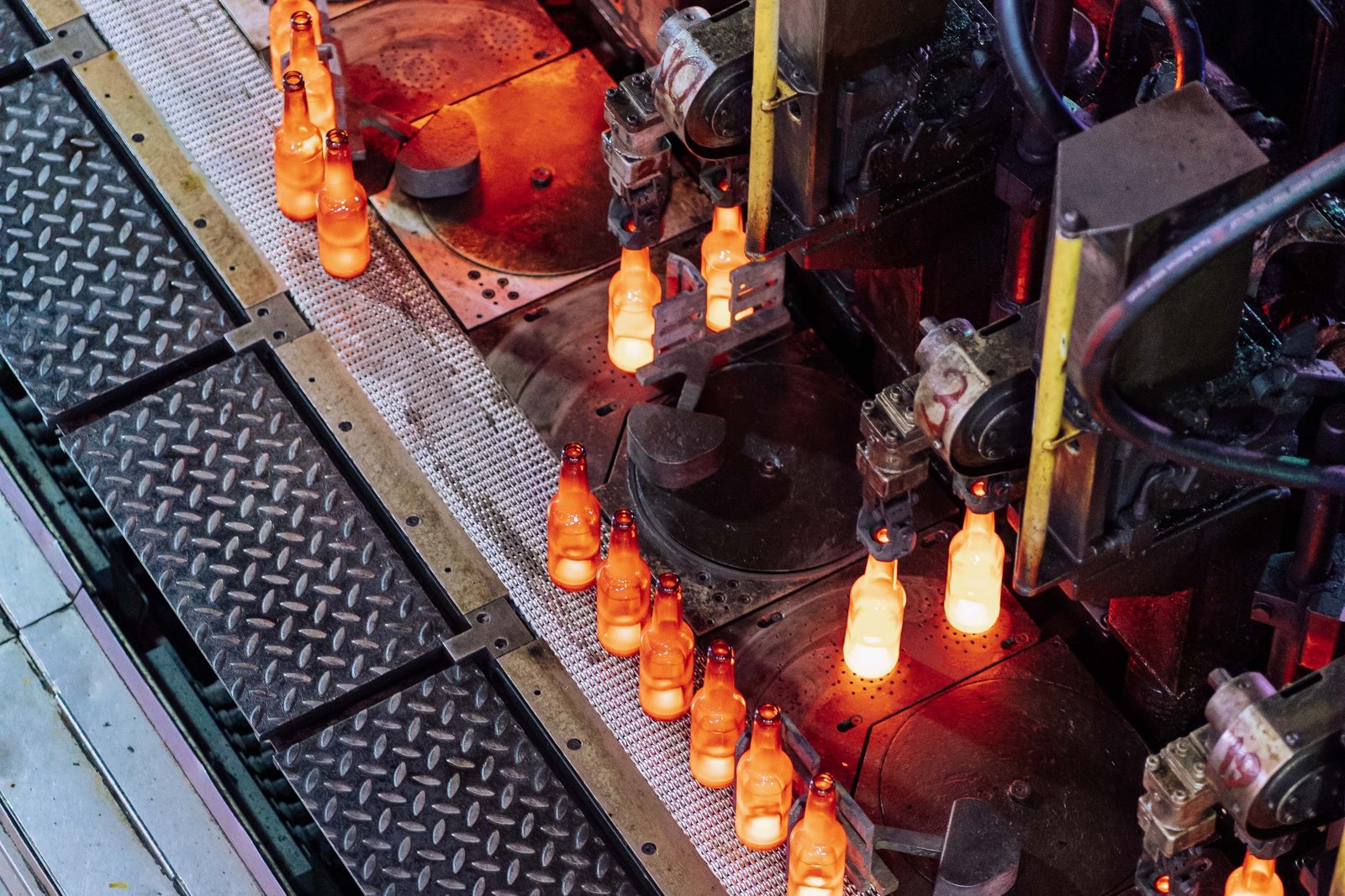 Newly formed glass bottles glowing as they move through machinery on an industrial production line.